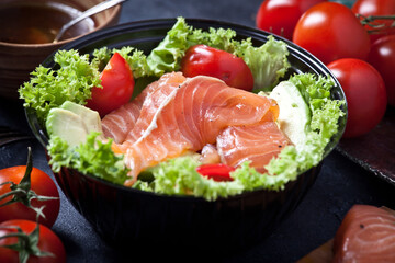 fresh salmon salad with avocado and lettuce leaves, sauce and fresh cherry tomatoes, closeup