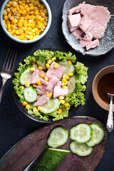fresh tuna salad with corn and lettuce leaves, sauce and fresh cucumbers, flatlay