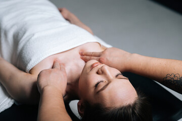 Obraz na płótnie Canvas Close-up top view of young woman lying down on massage table with closed eyes during shoulder and neck massage at spa salon. Male masseur professionally massaging shoulders on black background.