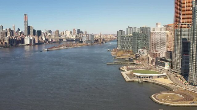 A high angle view looking north over the East River on a sunny day. The drone camera truck right and pan left, looking up the river to the Upper East side of Manhattan.