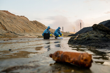 Two ecologists in rubber gloves, protective coveralls, eyeglasses and respirators studying...