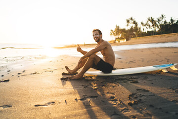 Portrait of cheerful surfer guy posing at professional surfboard enjoying sportive goals during...
