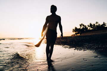 Silhouette of male spending evening for surfing during summer twilight at Carribean sea, amateur...