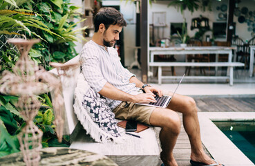 Focused man working on laptop near swimming pool