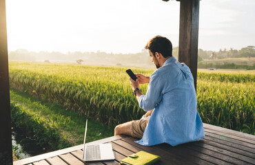Focused man browsing smartphone while working on laptop outdoors