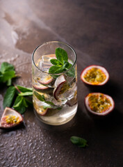 refreshing drink with passion fruit. cocktail with tropical fruit on a dark background. with green mint leaves. vertical position