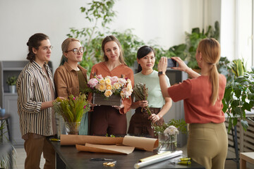 Diverse group of young florists florist holding floral composition while posing for photo in flower...