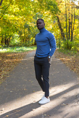Fototapeta premium Cheerful african american young man in stylish clothes walks in autumn park on sunny warm autumn day. Concept of weekend and outdoor recreation