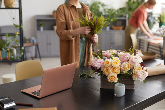Background image of open laptop on table in flower shop with unrecognizable female florist in background, copy space