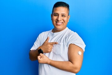 Young latin man using glucose meter button smiling happy pointing with hand and finger