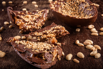 Stuffed chocolate easter egg with peanut and caramel on a wooden table with lots of peanuts around. Cracked.
