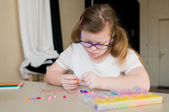 Cute Teen Girl Stringing Beads And Making Bracelet. Down Syndrome Kid Crafting Jewelry And Threading Bugle Beads. Play And Development Of Capacity Disability Children