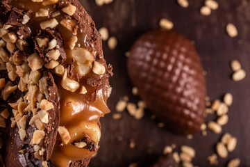 Close up of a stuffed chocolate easter egg with peanut and caramel on a wooden table with lots of peanuts around. Cracked. Top view. Selective focus.
