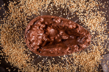 Stuffed chocolate easter egg with peanut and caramel on a wooden table with lots of peanuts around. Top view.