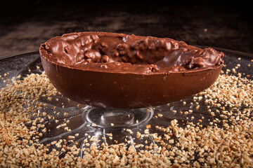 Stuffed chocolate easter egg with peanut and caramel on a wooden table with lots of peanuts around.