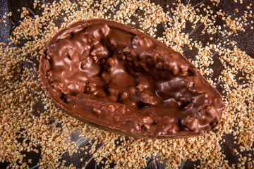 Stuffed chocolate easter egg with peanut and caramel on a wooden table with lots of peanuts around.