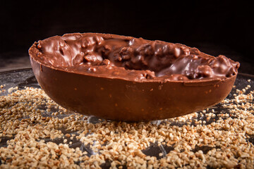 Stuffed chocolate easter egg with peanut and caramel on a wooden table with lots of peanuts around.