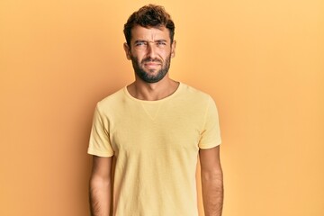 Handsome man with beard wearing casual yellow tshirt over yellow background skeptic and nervous, frowning upset because of problem. negative person.