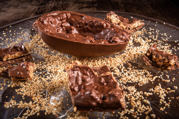 Stuffed chocolate easter egg with peanut and caramel on a wooden table with lots of peanuts around.