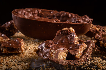 Stuffed chocolate easter egg with peanut and caramel on a wooden table with lots of peanuts around.