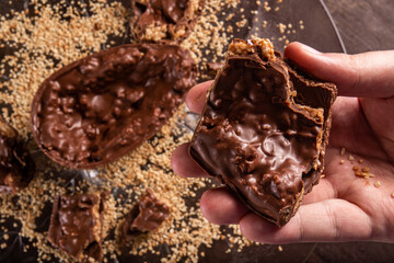 Hand takes a stuffed chocolate easter egg with peanut and caramel on a wooden table with lots of...