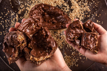 Hand takes a stuffed chocolate easter egg with peanut and caramel on a wooden table with lots of peanuts around. Top view.