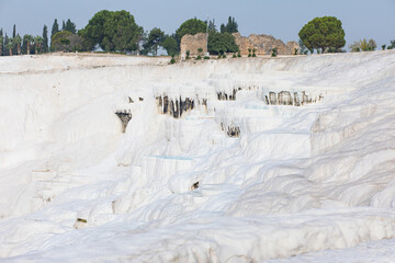 Bowls of water, travertines, white walls of Pamukkale mountain in Turkey with an ancient ruined antique brick wall on top.