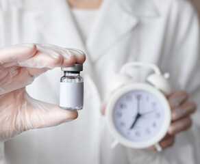 Doctor's hand holding bottle for vaccine and alarm clock. Development and creation vaccines. Vaccination against influenza, viruses, infections. Selective focus