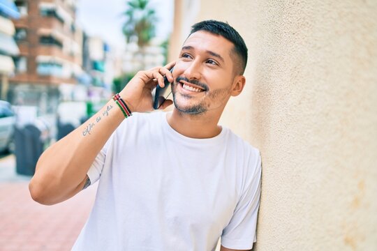 Young hispanic man smiling happy talking on the smartphone leaning on the wall.