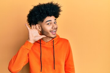 Fototapeta na wymiar Young african american man with afro hair wearing casual sweatshirt smiling with hand over ear listening and hearing to rumor or gossip. deafness concept.