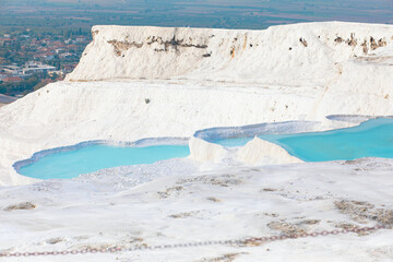 Wonderful turquoise blue travertine baths with water in of white mountain Pamukkale in Turkey.