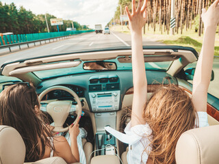 Portrait of two young beautiful and smiling hipster female in convertible car. Sexy carefree women...