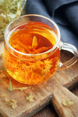 Linden herbal tea with flowers in a glass cup on wooden rustic board with lime blossom dry herb nearby, closeup, drink for relaxation, mental health,  naturopathy, homeopathy and folk medicine concept