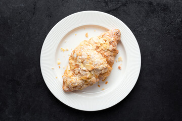 Sweet almond croissant on white plate, black concrete background, top view. French pastry