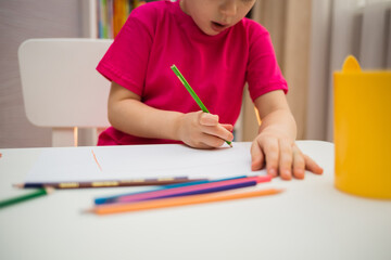 close-up of a child drawing with a pencil on a white sheet of paper