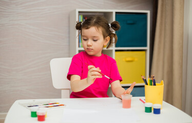 a little girl sits at a table with paints and brushes