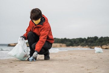 Volunteer picking up disposable masks and gloves and trash on the beach during coronavirus outbreak - Focus on right hand