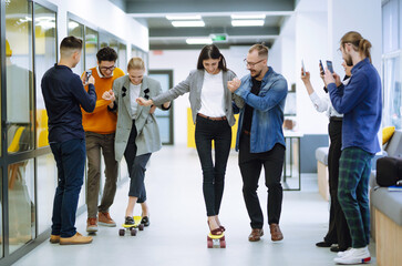 Group of coworkers having fun with skateboard in the office. Business people cheering when their colleagues skateboarding in the office. 