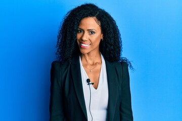 Middle age african american woman using lavalier microphone looking positive and happy standing and...