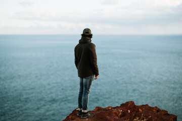 Man with cap and black jacket looking at the ocean from a rock in Tenerife. Hiking and lifestyle © Marcos