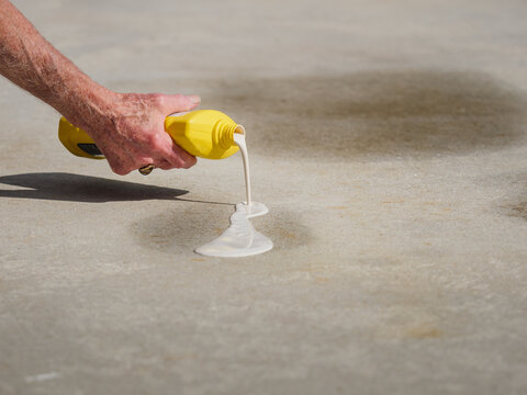 Man applying oil stain remover to concrete driveway. Removing automobile motor oil stains from parking spots with cleaning product.