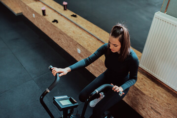 Fototapeta na wymiar Serious caucasian female in activewear sitting on exercising bike ready for reaching good results in cardiom