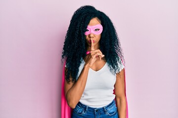 Middle age african american woman wearing super hero costume asking to be quiet with finger on...