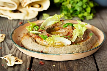 An oriental dish of baked eggplant babaganush (eggplant puree) with spices, herbs, lettuce and oriental flatbreads on wooden background.