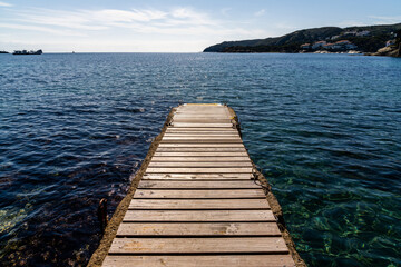 Obraz premium wood and concrete pier leading out into the clear refreshing waters of the Mediterranean Sea in a picturesque and peaceful cove