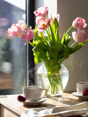Coffee for two at the table near the window with pink tulips