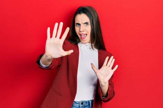 Young brunette teenager wearing business jacket afraid and terrified with fear expression stop gesture with hands, shouting in shock. panic concept.