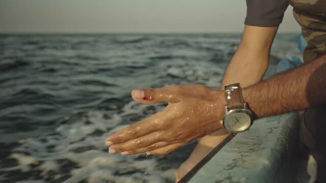 Fisherman Washing Hands With Sea Water Off Side Of Moving Boat. Tracking Shot