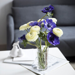 Bouquet of white ranunculus and blue anemone in the vase on a white coffee table near sofa with...