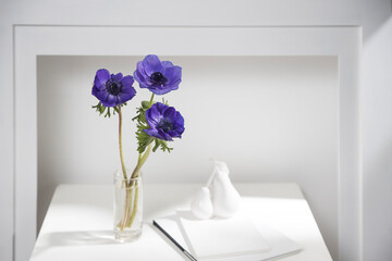 Bouquet of blue anemone in the vase on a white coffee table next to the fake fireplace. Shadow.